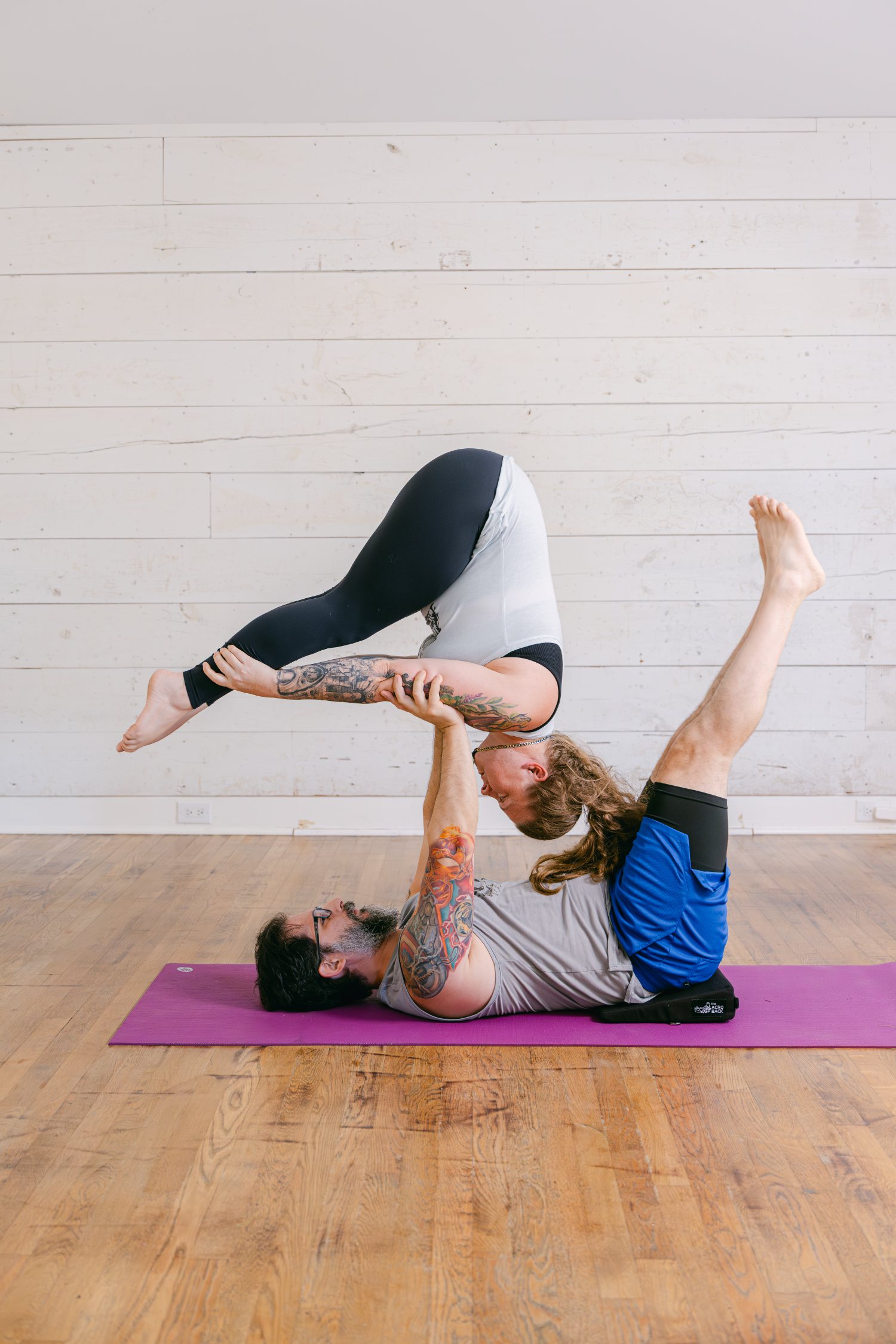Two students in a supported acro yoga pose, demonstrating alignment and trust